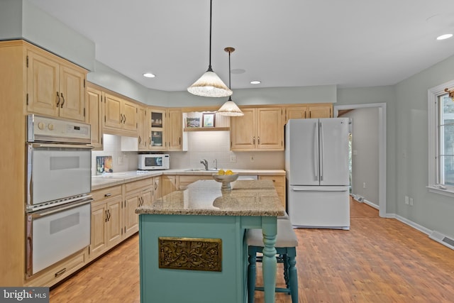 kitchen with white appliances, decorative backsplash, a kitchen island, glass insert cabinets, and light stone countertops