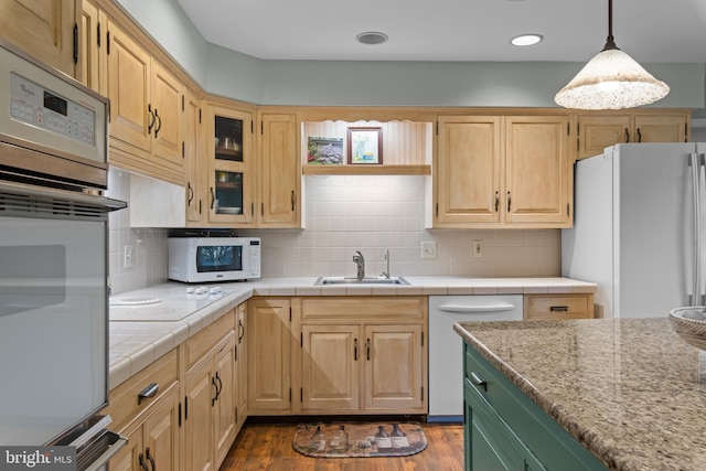 kitchen featuring white appliances, a sink, light countertops, hanging light fixtures, and glass insert cabinets