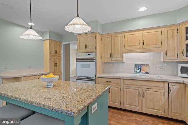 kitchen featuring white appliances, a kitchen island, light wood-type flooring, tasteful backsplash, and pendant lighting