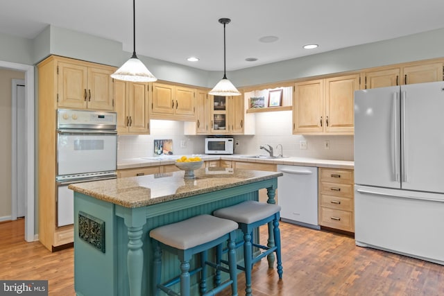 kitchen featuring white appliances, a sink, a kitchen island, light stone countertops, and light brown cabinetry