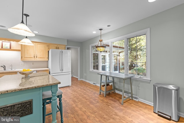 kitchen with a sink, hanging light fixtures, light brown cabinets, and freestanding refrigerator