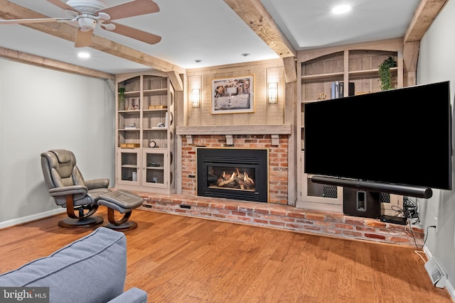 living room with built in features, a brick fireplace, wood finished floors, beamed ceiling, and baseboards