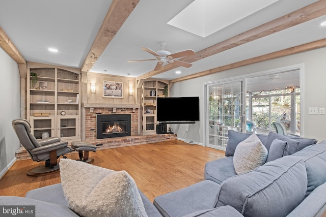 living area with a brick fireplace, beamed ceiling, baseboards, and wood finished floors