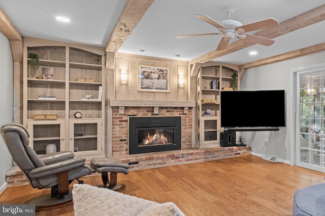 living room featuring beam ceiling, a fireplace, visible vents, wood finished floors, and baseboards