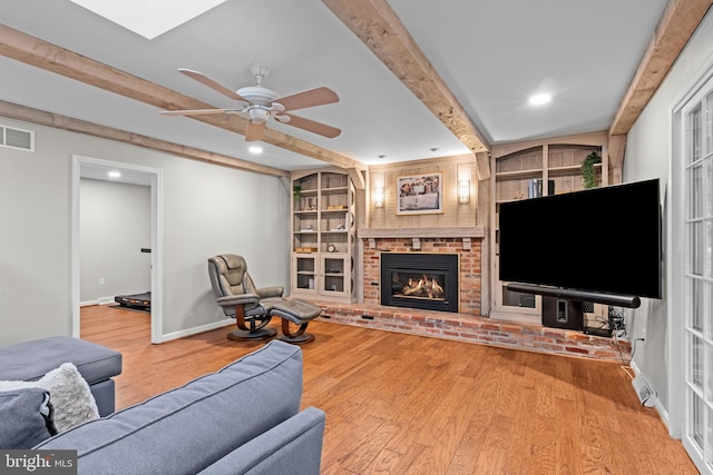 living room featuring baseboards, visible vents, beamed ceiling, light wood-type flooring, and a fireplace