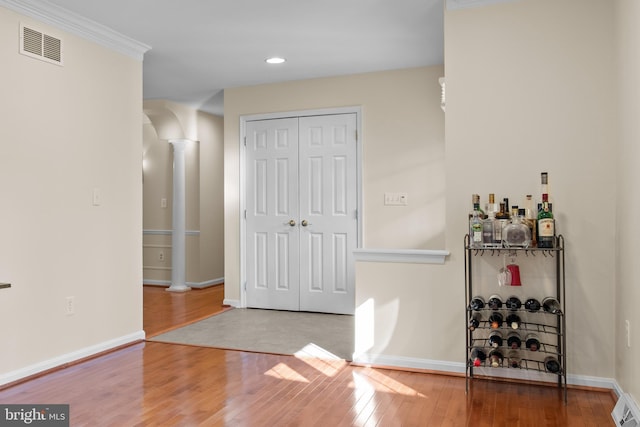 bar with decorative columns, wood-type flooring, visible vents, ornamental molding, and baseboards