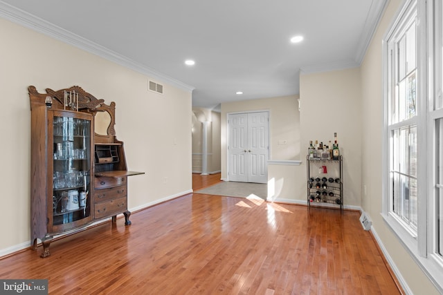 living area featuring a healthy amount of sunlight, visible vents, crown molding, and wood finished floors