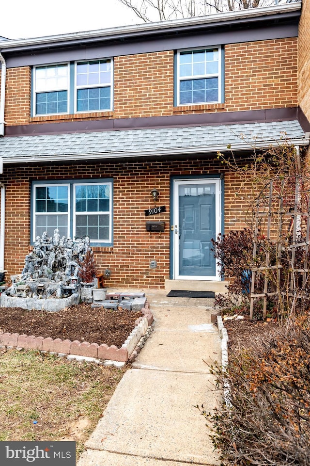 entrance to property featuring a shingled roof and brick siding