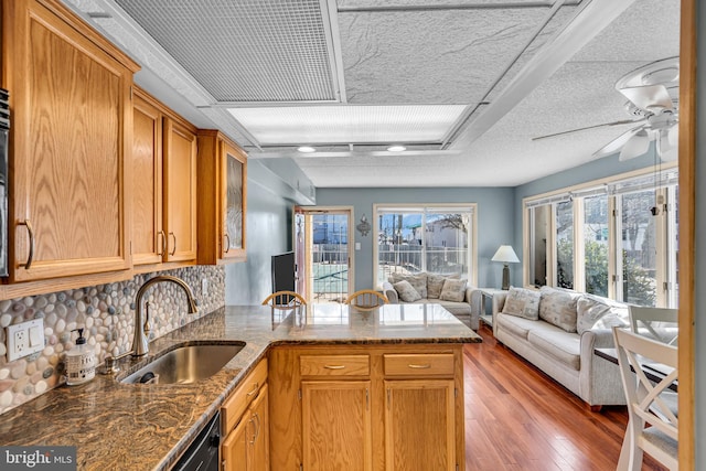 kitchen with open floor plan, a peninsula, stone countertops, and a sink