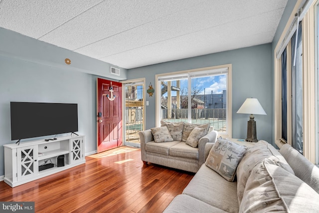 living room with dark wood-style flooring, visible vents, and baseboards