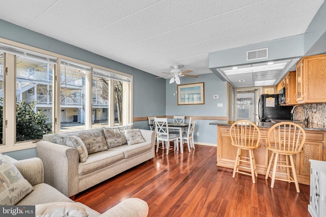 living area with dark wood-type flooring, visible vents, ceiling fan, and baseboards