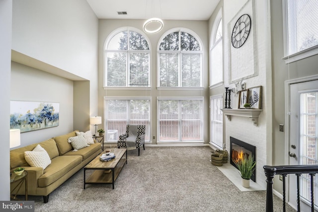 living room featuring carpet, a high ceiling, a fireplace, visible vents, and plenty of natural light