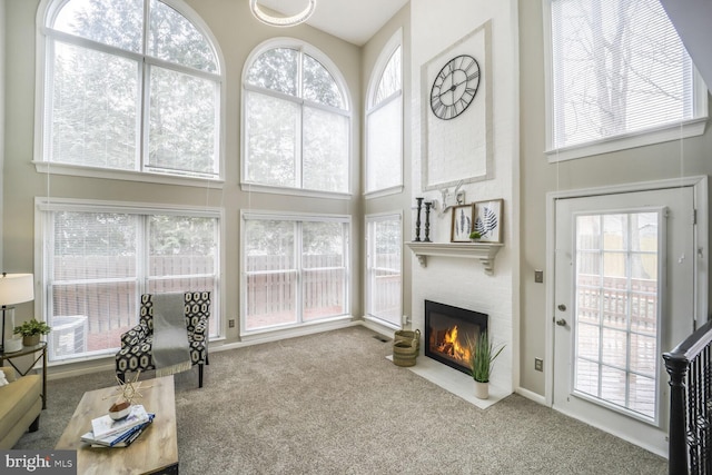 carpeted living area featuring a healthy amount of sunlight, a fireplace, and a high ceiling