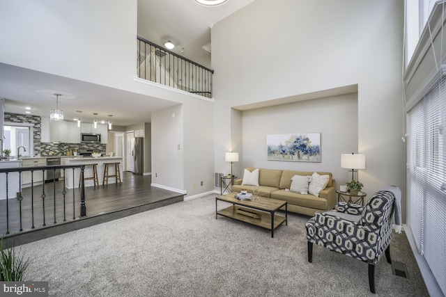 living room with carpet floors, visible vents, a towering ceiling, and baseboards