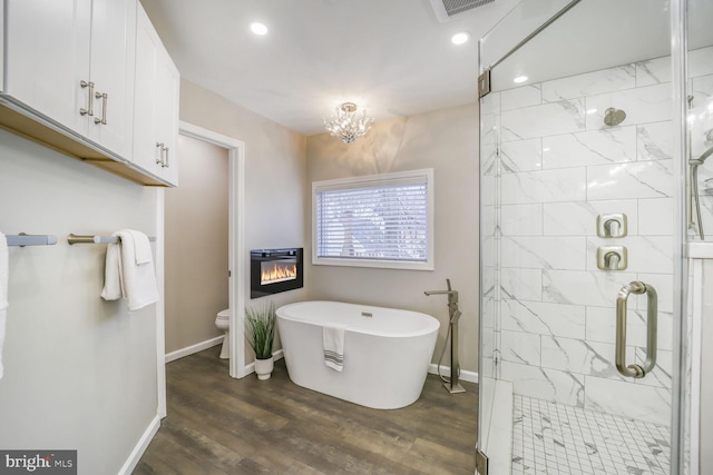 bathroom with a soaking tub, a glass covered fireplace, a shower stall, wood finished floors, and baseboards