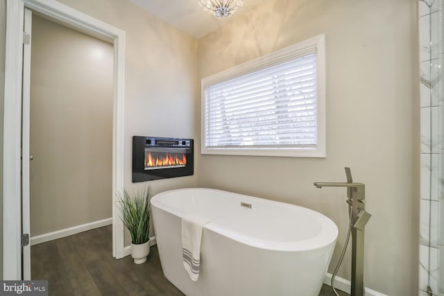 bathroom with a glass covered fireplace, a soaking tub, baseboards, and wood finished floors