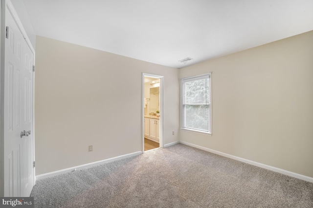 unfurnished bedroom featuring ensuite bath, carpet, visible vents, and baseboards