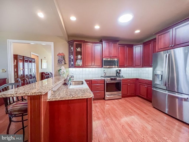 kitchen with decorative backsplash, a breakfast bar, a peninsula, stainless steel appliances, and a sink