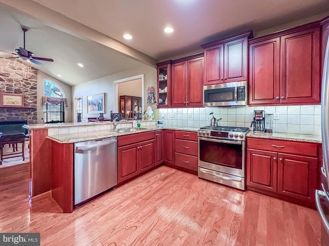 kitchen featuring stainless steel appliances, a peninsula, a sink, light wood-style floors, and backsplash