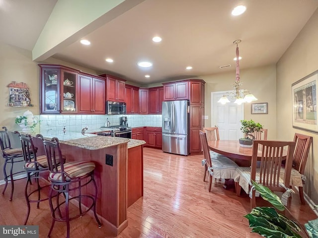 kitchen featuring backsplash, appliances with stainless steel finishes, light wood-style floors, glass insert cabinets, and a peninsula