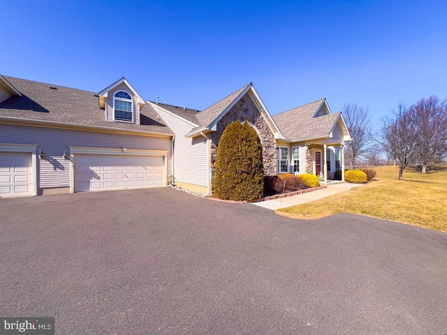 view of front of house with a front yard, stone siding, roof with shingles, and driveway