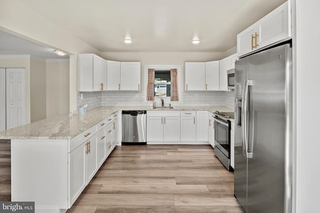 kitchen featuring stainless steel appliances, light wood-style flooring, white cabinets, a sink, and a peninsula