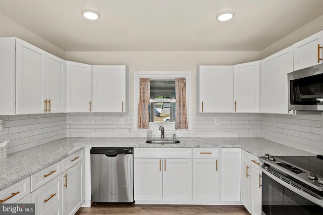 kitchen with appliances with stainless steel finishes, light stone counters, a sink, white cabinetry, and backsplash