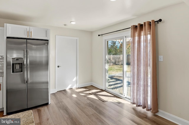 kitchen with baseboards, light wood finished floors, stainless steel fridge with ice dispenser, and white cabinetry