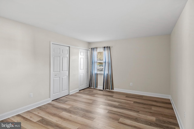 unfurnished bedroom with light wood finished floors, baseboards, and a closet