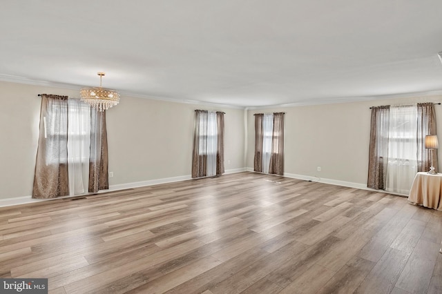 spare room with ornamental molding, wood finished floors, a wealth of natural light, and an inviting chandelier