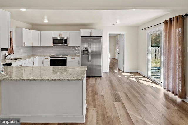 kitchen with light stone countertops, white cabinetry, appliances with stainless steel finishes, and light wood-style floors