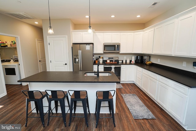 kitchen featuring washer / dryer, a center island with sink, dark countertops, appliances with stainless steel finishes, and white cabinetry