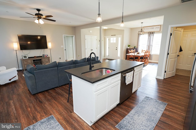 kitchen with dark countertops, open floor plan, a kitchen island with sink, white cabinetry, and a sink