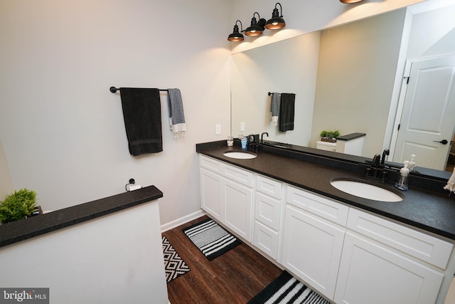 full bath featuring double vanity, baseboards, a sink, and wood finished floors