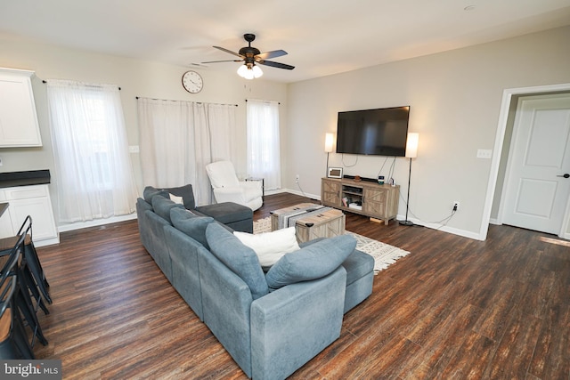 living area with a ceiling fan, baseboards, dark wood finished floors, and a wealth of natural light