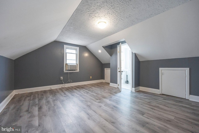 additional living space with baseboards, wood finished floors, vaulted ceiling, cooling unit, and a textured ceiling