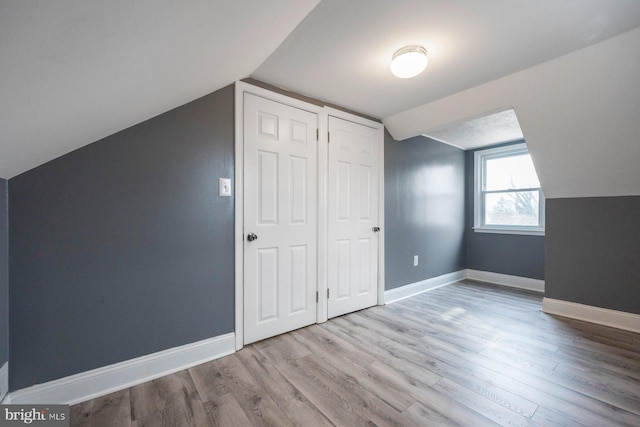 additional living space with light wood-style floors, baseboards, and vaulted ceiling