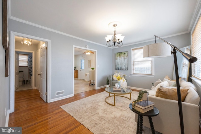 living area with crown molding, visible vents, wood finished floors, a chandelier, and baseboards