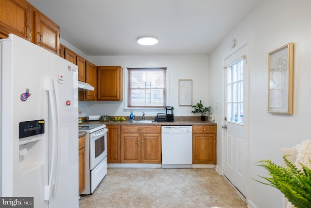 kitchen featuring under cabinet range hood, white appliances, a sink, brown cabinetry, and dark countertops