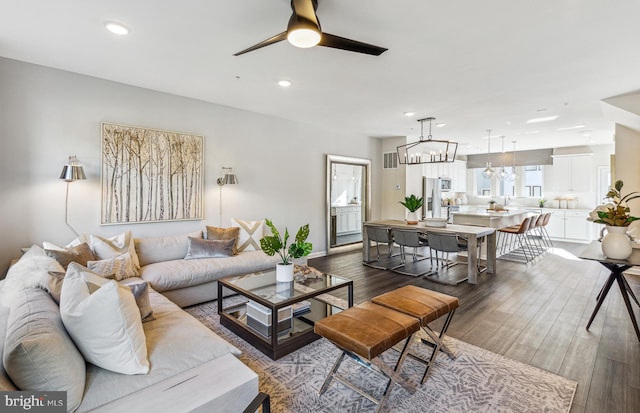 living room featuring ceiling fan with notable chandelier, dark wood finished floors, visible vents, and recessed lighting