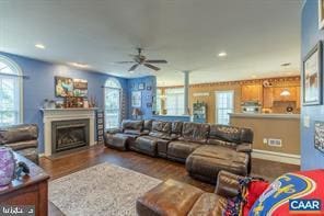 living room featuring dark wood finished floors, a fireplace with raised hearth, plenty of natural light, and ceiling fan