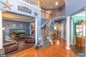 interior space with a towering ceiling, decorative columns, stairway, and wood finished floors