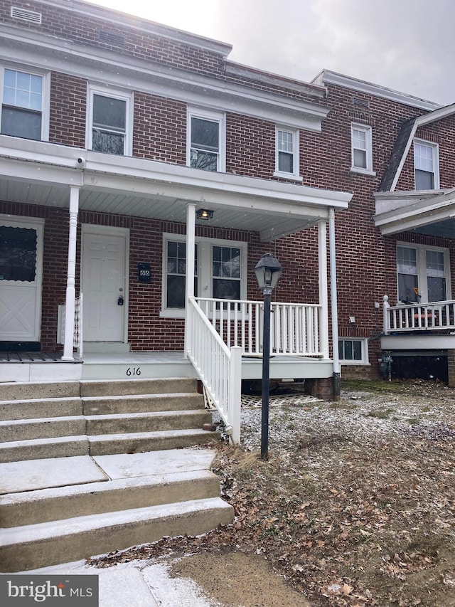 view of exterior entry featuring a porch and brick siding