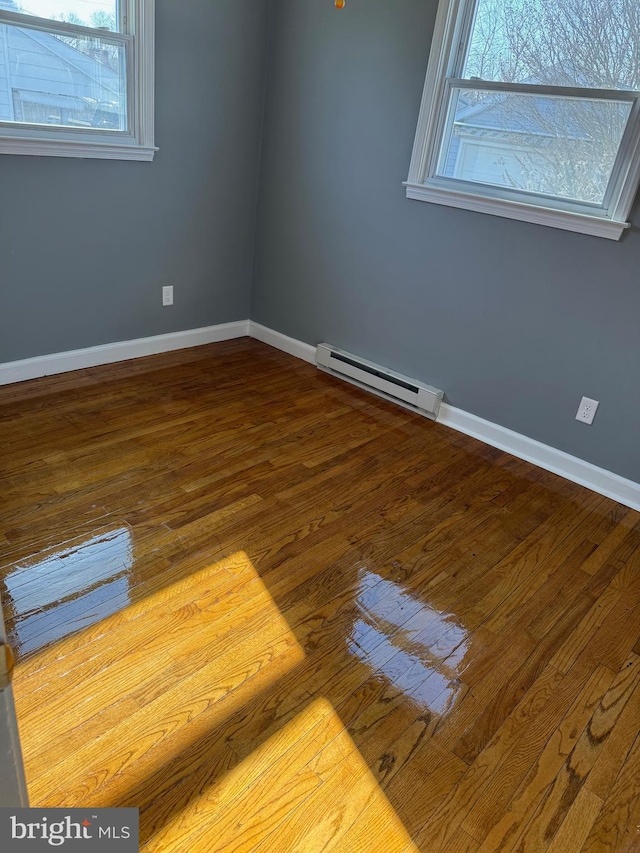 empty room with baseboard heating, wood finished floors, and baseboards