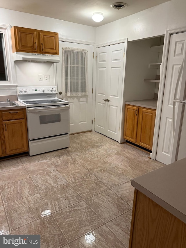 kitchen with brown cabinets, visible vents, under cabinet range hood, and white range with electric cooktop