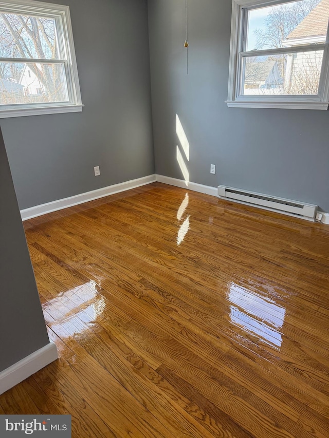 unfurnished room featuring a baseboard radiator, baseboards, and wood finished floors