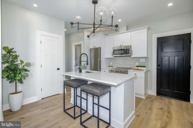 kitchen featuring decorative backsplash, appliances with stainless steel finishes, white cabinets, a sink, and an island with sink