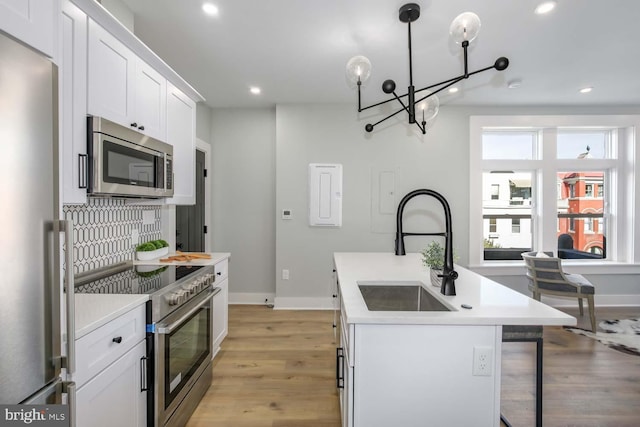 kitchen featuring decorative backsplash, an island with sink, stainless steel appliances, white cabinetry, and a sink