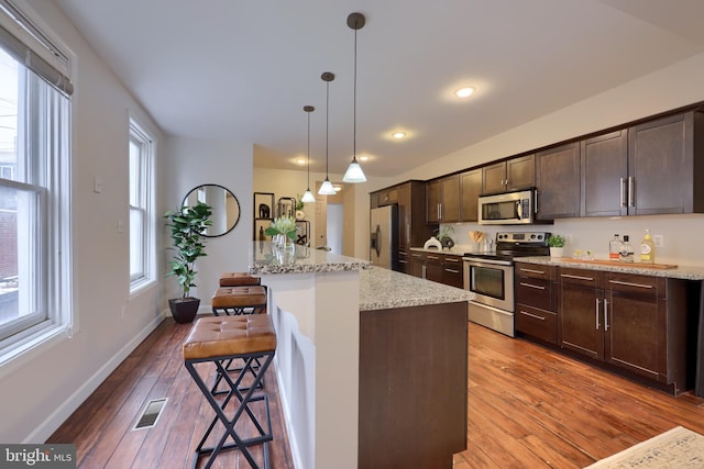 kitchen with a breakfast bar, pendant lighting, a center island with sink, stainless steel appliances, and light stone countertops