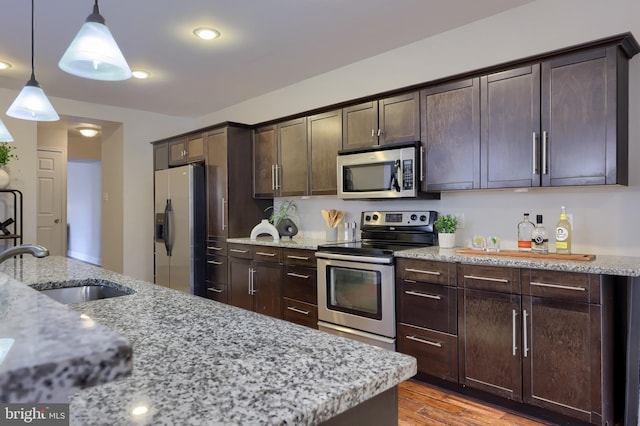 kitchen with stainless steel appliances, decorative light fixtures, a sink, and dark brown cabinets